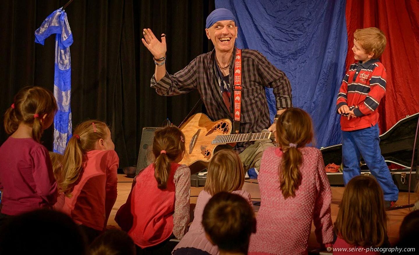 Mann spielt mit Gitarre für Kinder bei einem Konzert