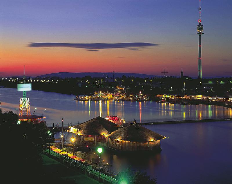 Beleuchteter Donauturm bei Nacht. Im Vordergrund sieht man die "Sunken City" und ihre Lokale.