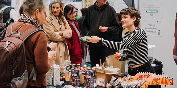 Besucher bei einem Messestand, Ausstellerin präsentiert Produkte