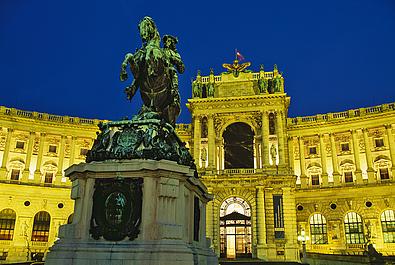 Die beleuchtete Neue Burg bei Nacht - im Vordergrund ein Denkmal.