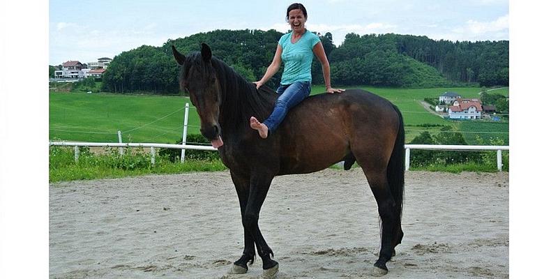 Frau sitzt auf dunklem Pferd und lächelt