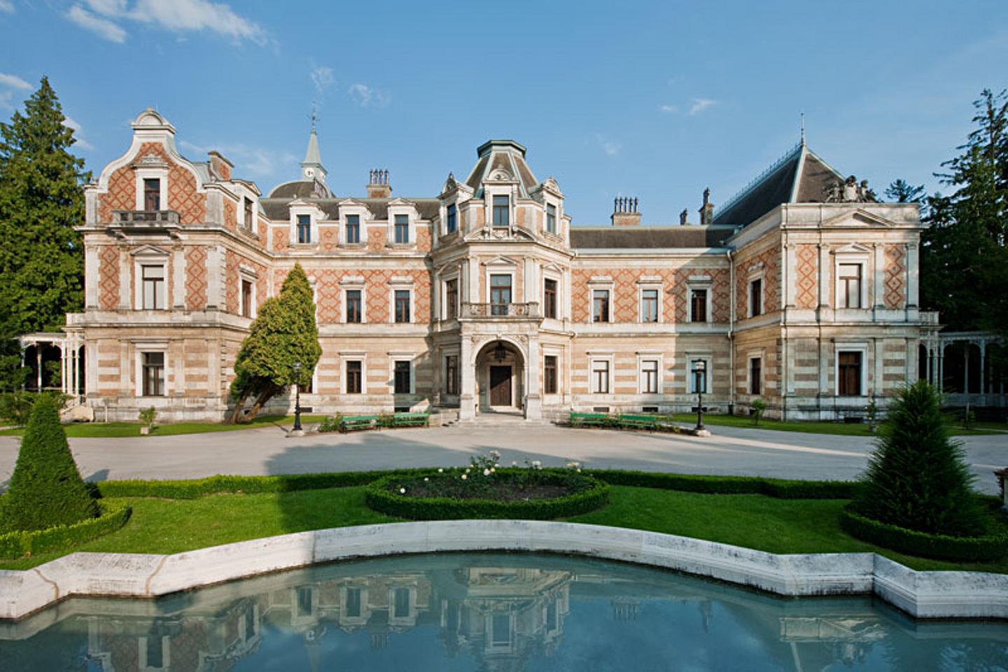 Ansicht auf eien prächtige Villa mit großer auffahrt, Wiese und Wasserbecken.