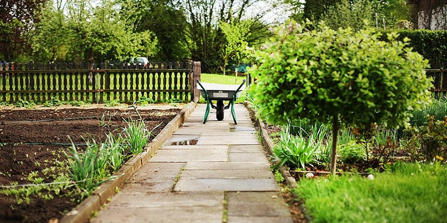 Scheibtruhe steht auf einem Weg mitten in einem Garten