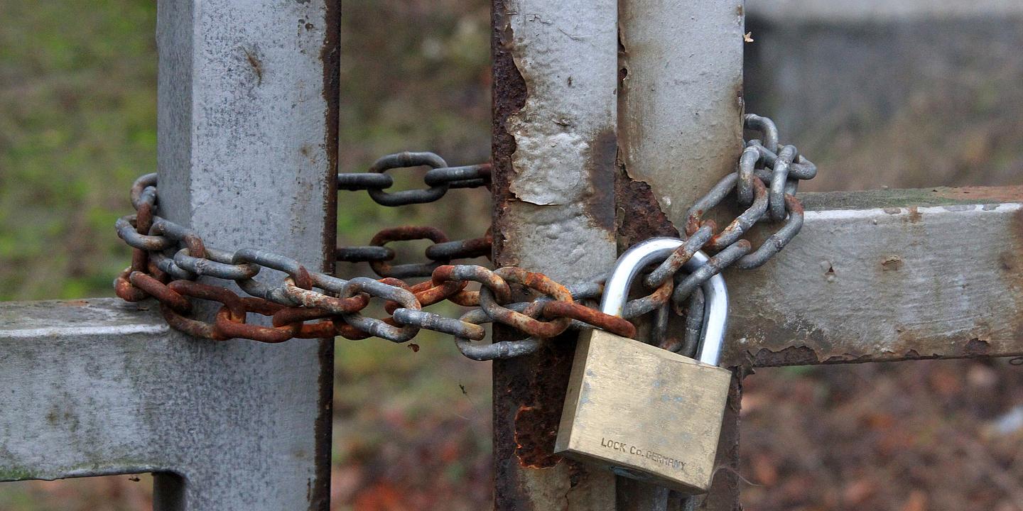 Mit Kette und Vorhangschloss versperrter Zaun bzw. Zugang zu einem Grundstück.