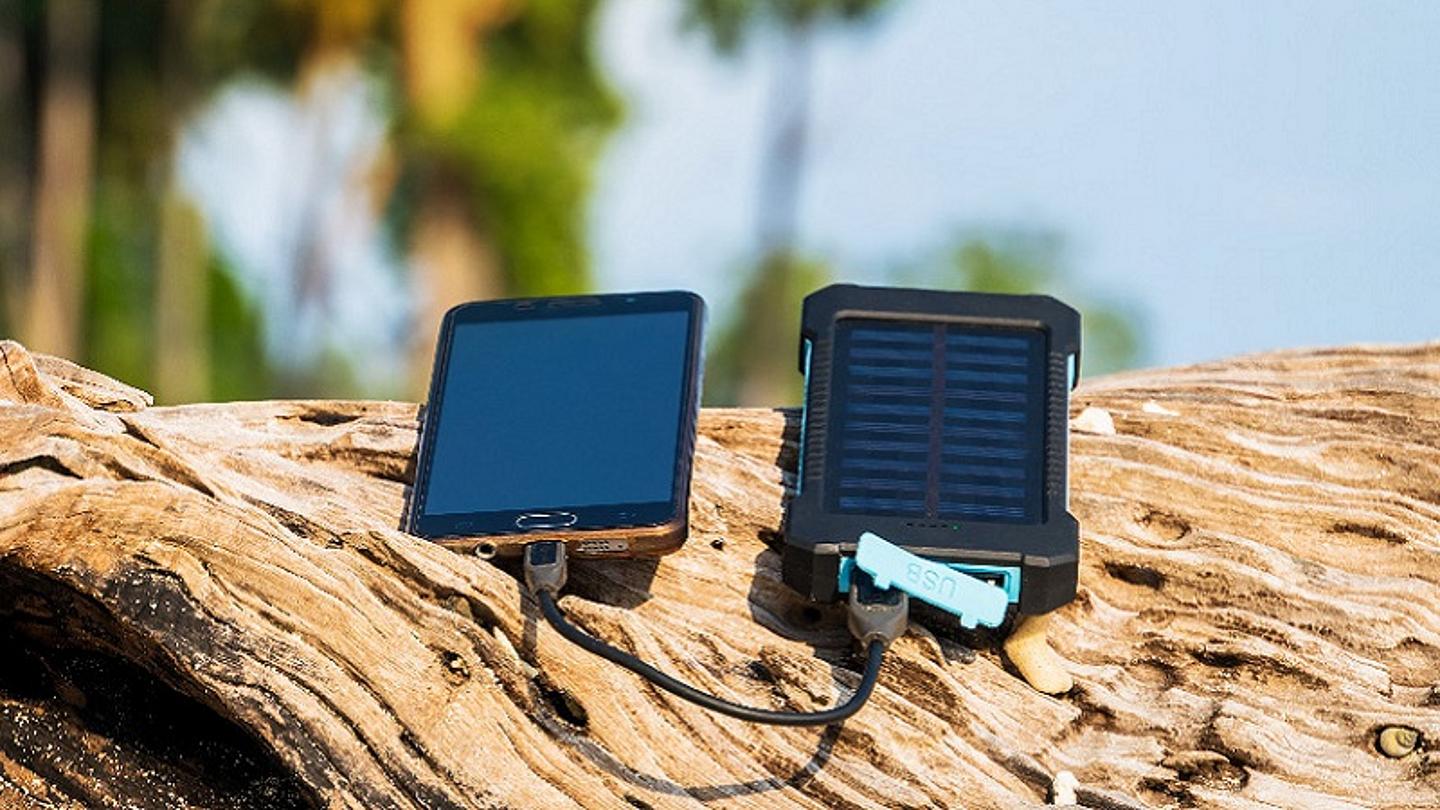 Solar Powerbank an der ein Handy angeschlossen ist liegt auf Baumstamm