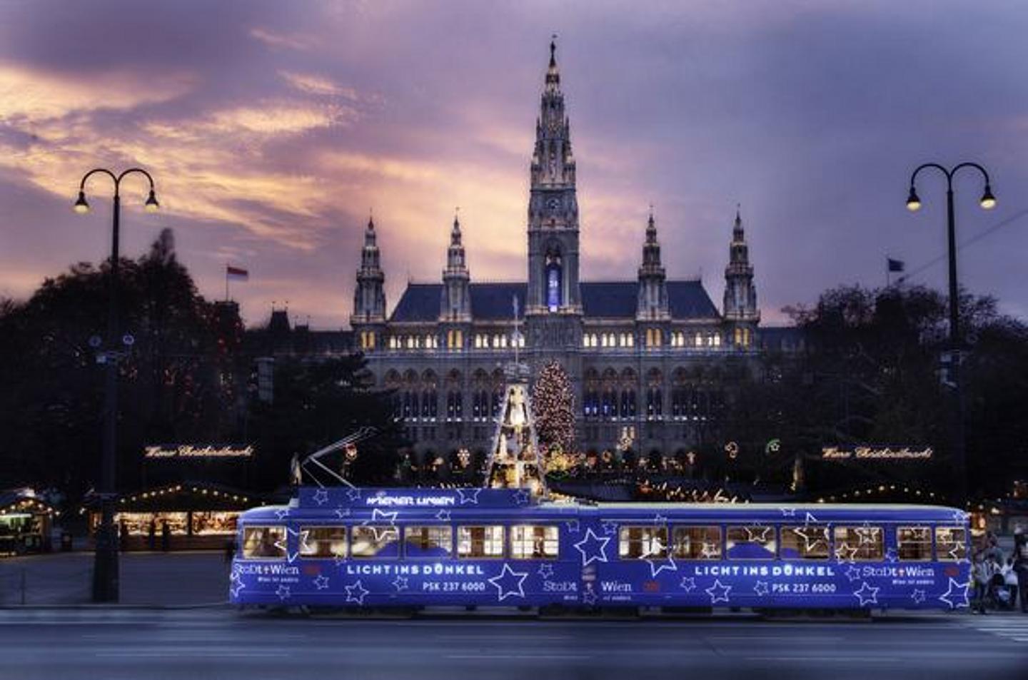 Der Rathausplatz in Wien in der vorweihnachtszeit mit violetter Straßenbahn im Vordergrund.