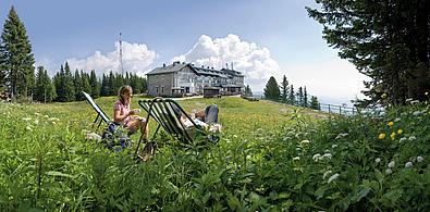 Mann und Frau auf Bergwiese im Hintergrund ein Haus