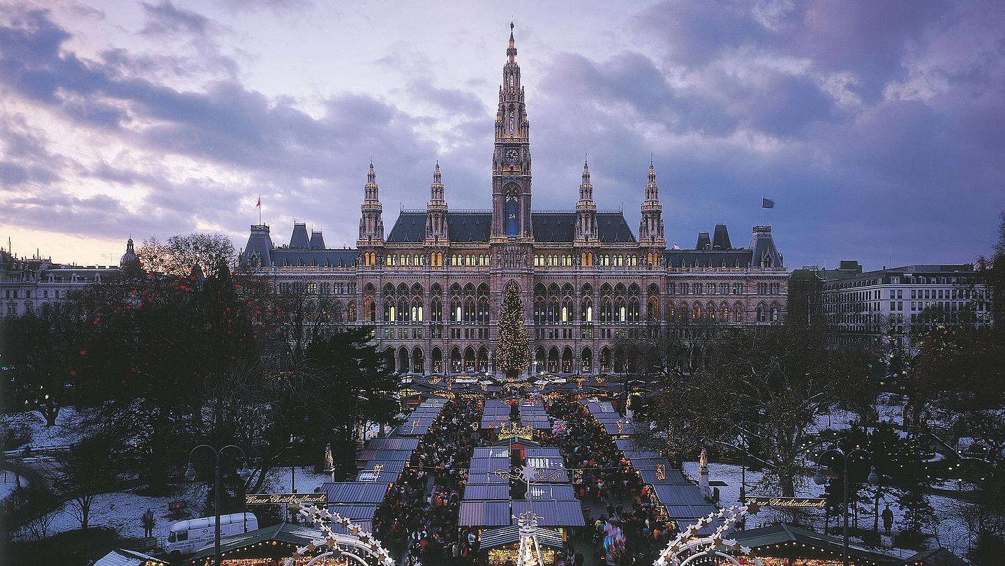 Bild von Weihnachtsmarkt vorm Wiener Rathaus bei Abenddämmerung.