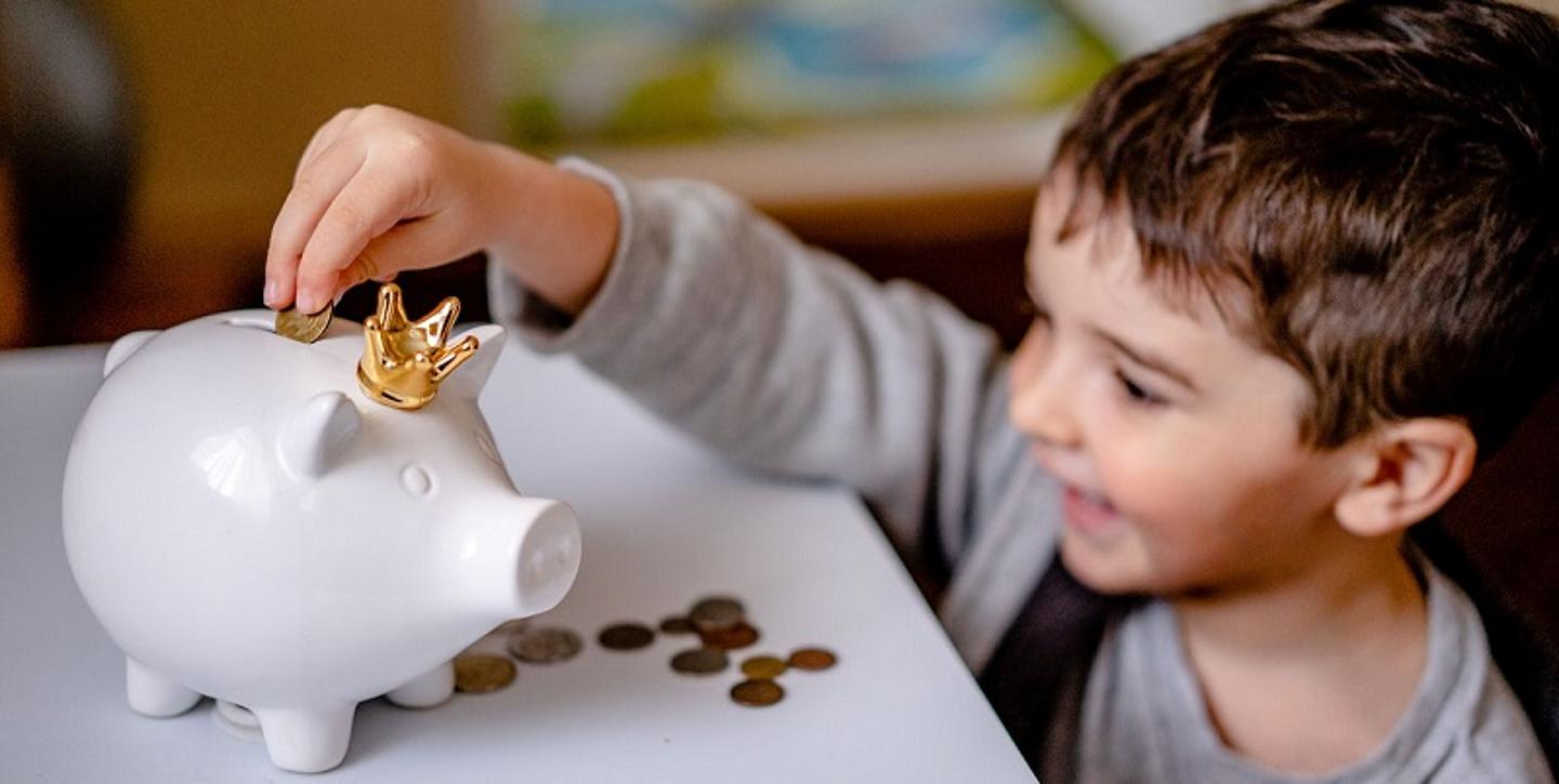 Das Bild zeigt einen Jungen, der Geld in ein Sparschwein einwirft. 