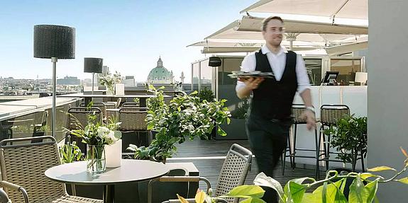 Ein Kellner mit Tablett geht über die Dachterrasse eines Lokals