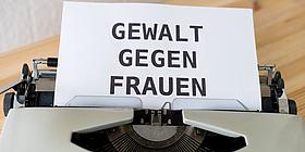 Das Bild zeigt ein Blatt in einer Schreibmaschine mit der Aufschrift "Gewalt gegen Frauen". 