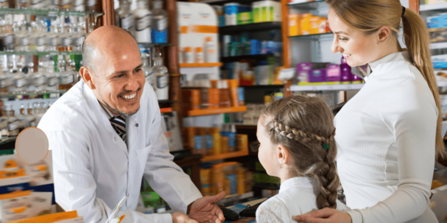 Ein Apotheker bedient zwei Kunden in seiner Apotheke. Die Kunden sind ein kleines Mädchen und ihre Mutter