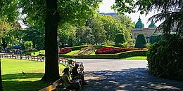 Eingang zum Stadtpark Wien mit Sitzbänken, im Hintergrund die Blumenuhr