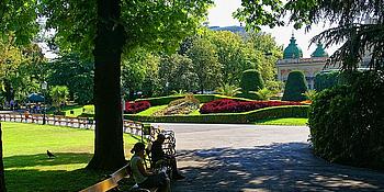 Eingang zum Stadtpark Wien mit Sitzbänken, im Hintergrund die Blumenuhr