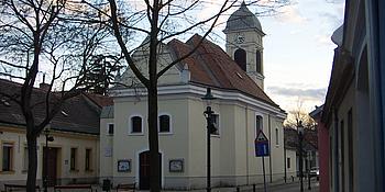 Bild von Kirche in Groß-Jedlersdorf und ihrem Vorplatz, auf dem ein paar Parkbänke stehen.