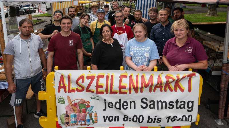 Menschen die Banner von Alszeilenmarkt in die Kamera halten