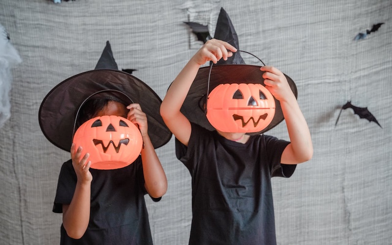 Zwei Kinder in Hexenkostümen mit Kürbislampen. 