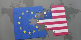 Die Flaggen der EU und der USA als Puzzle bei dem einige Teile fehlen. Im Hintergrund eine Weltkarte