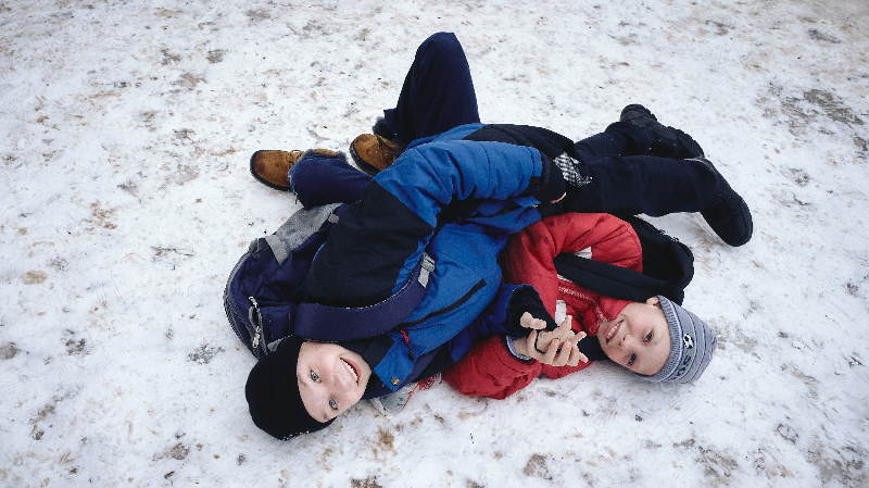 Zwei Jungs die im Skianzug im Schnee herumtollen