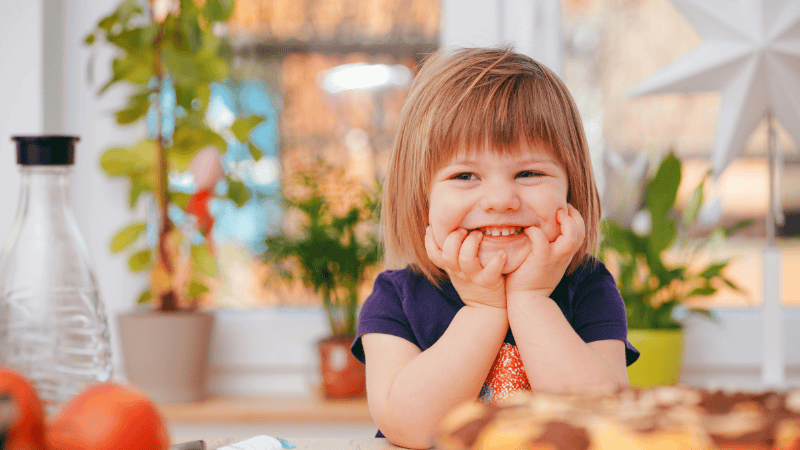 ein lächelndes Mädchen sitzt am Tisch und wartet auf ihr Essen