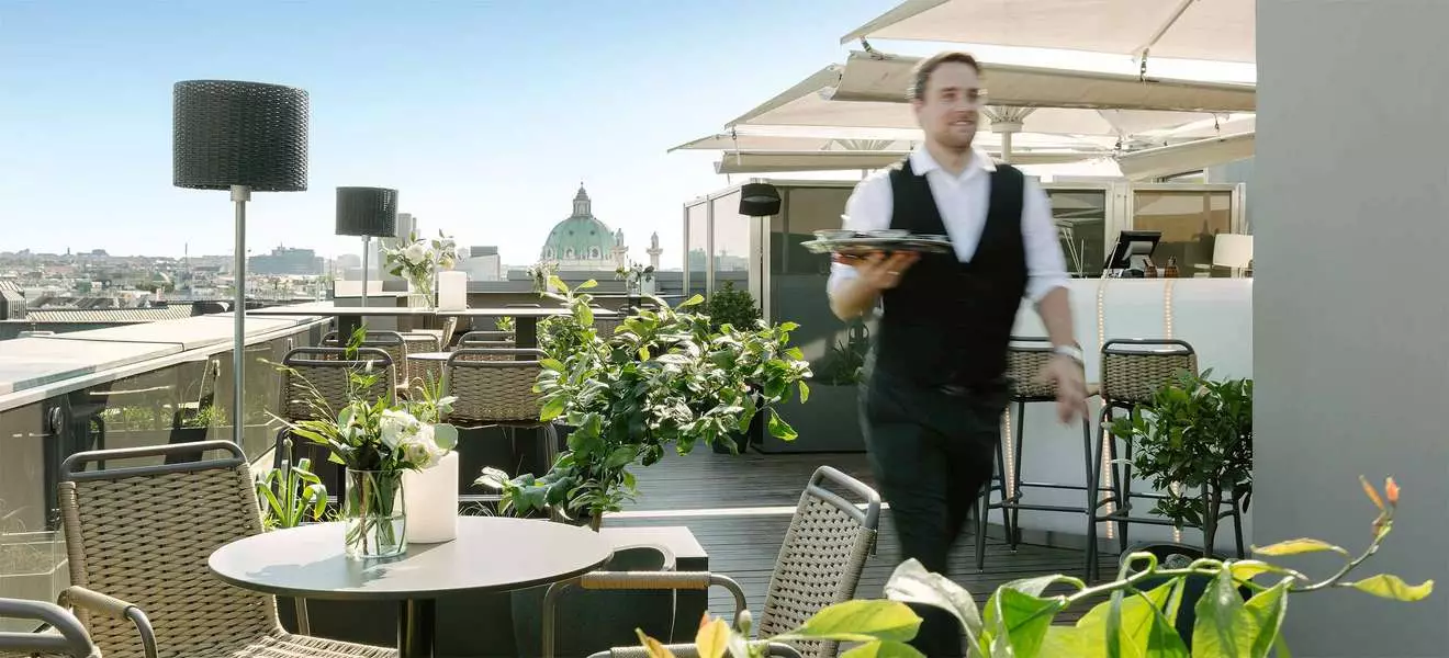 Ein Kellner mit Tablett geht über die Dachterrasse eines Lokals