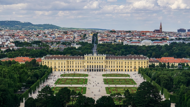 Landschaftsfoto, Blick von der Gloriette auf das Schloss Schönbrunn, im Hintergrund Stadtpanorama.