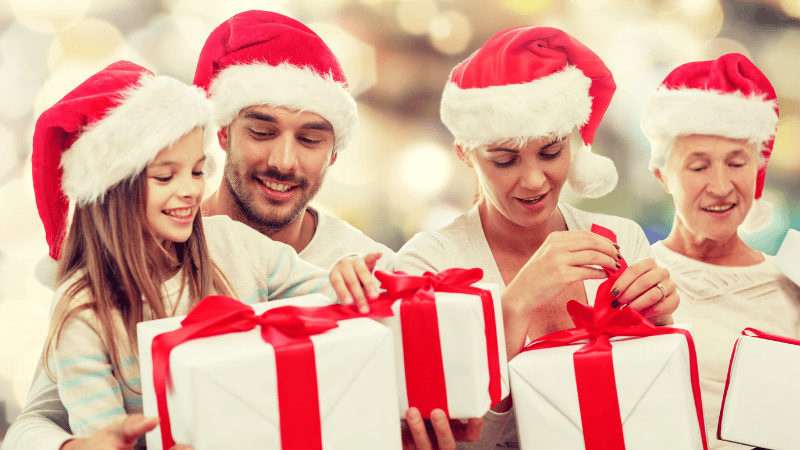 Eine vierköpfige Familie mit Weihnachtsmannmützen hält Geschenke und lächelt