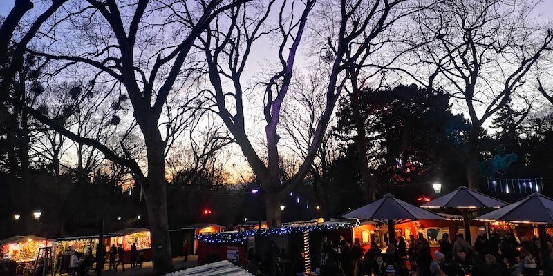 Dämmerung mit Baumschatten und beleuchteten Weihnachtsmarktständen