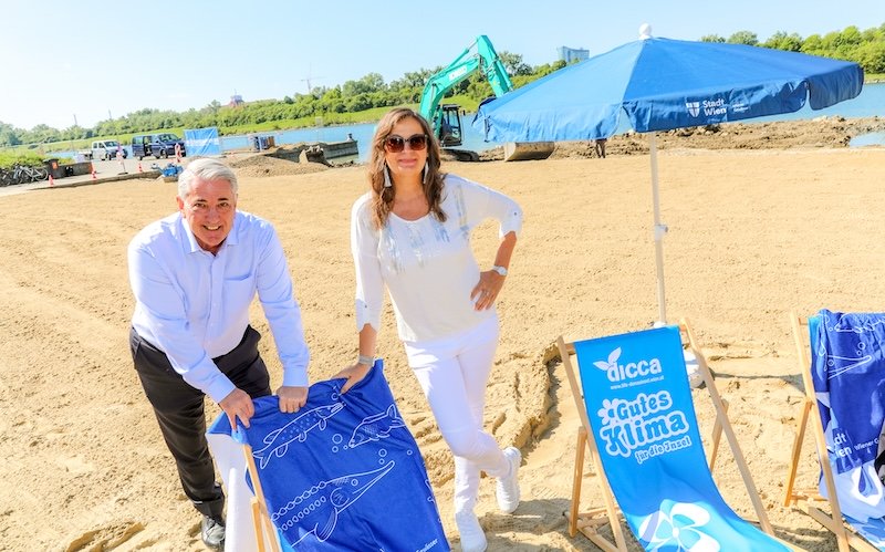 Bezirksvorsteher Ernst Nevrivy und Stadträtin Ulli Sima am Arena Beach mit Liegestühlen und Sonnenschirm.